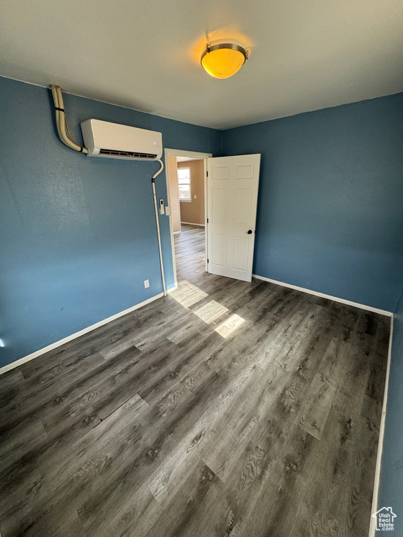 Unfurnished bedroom featuring baseboards, wood finished floors, and a wall mounted AC