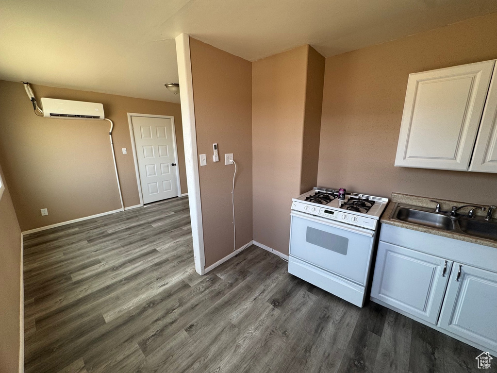 Kitchen with a sink, a wall unit AC, dark wood-style flooring, white cabinetry, and white range with gas stovetop