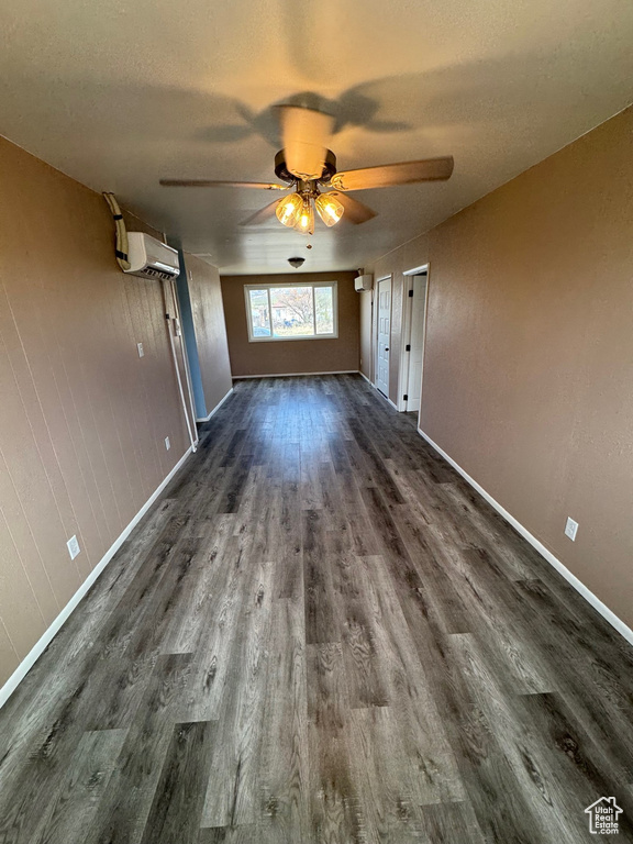 Unfurnished living room with a wall mounted air conditioner, ceiling fan, baseboards, and dark wood-type flooring