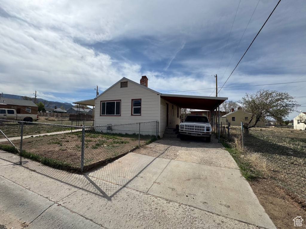 View of front facade featuring fence, driveway, a chimney, and an attached carport