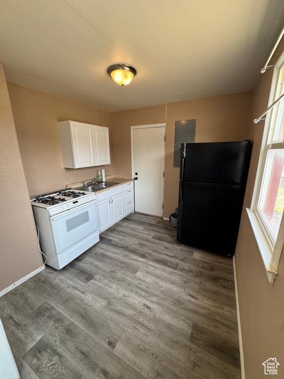 Kitchen featuring light wood finished floors, white cabinets, a sink, freestanding refrigerator, and white gas stove