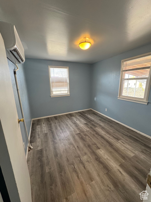 Empty room featuring a wall mounted AC, wood finished floors, a wealth of natural light, and baseboards