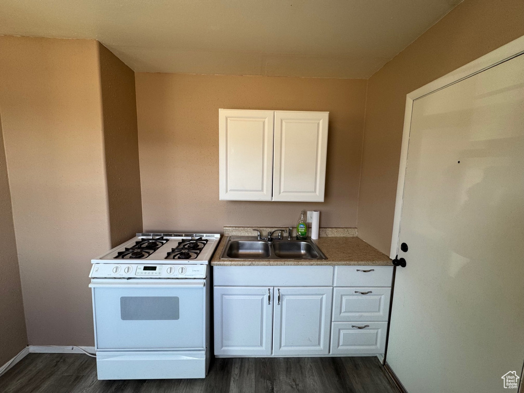 Kitchen featuring a sink, white range with gas stovetop, baseboards, white cabinetry, and dark wood-type flooring
