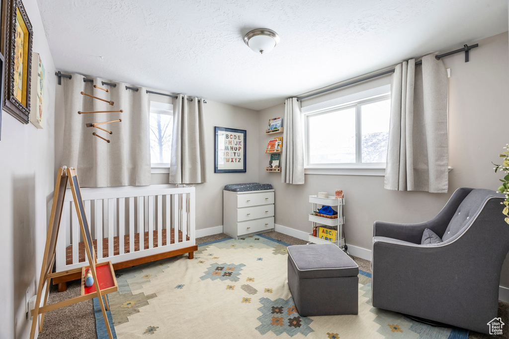 Bedroom featuring multiple windows, baseboards, a textured ceiling, carpet floors, and a crib