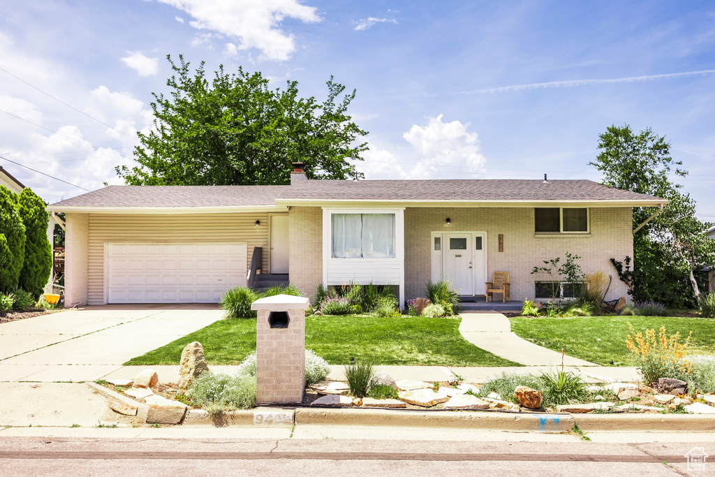 View of front facade with a garage, concrete driveway, a chimney, a front lawn, and brick siding
