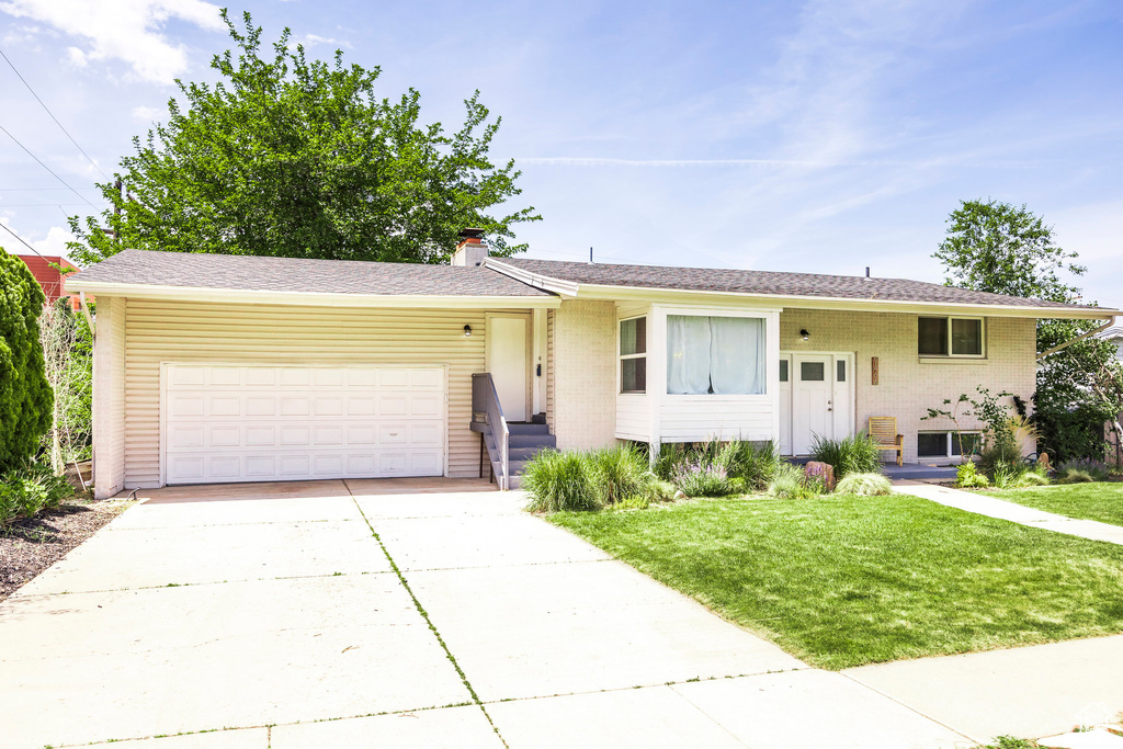 View of front facade with a garage, a front lawn, concrete driveway, a chimney, and brick siding