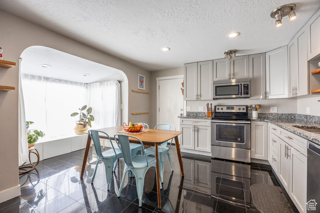 Kitchen featuring stainless steel appliances, open shelves, a sink, light stone counters, and recessed lighting