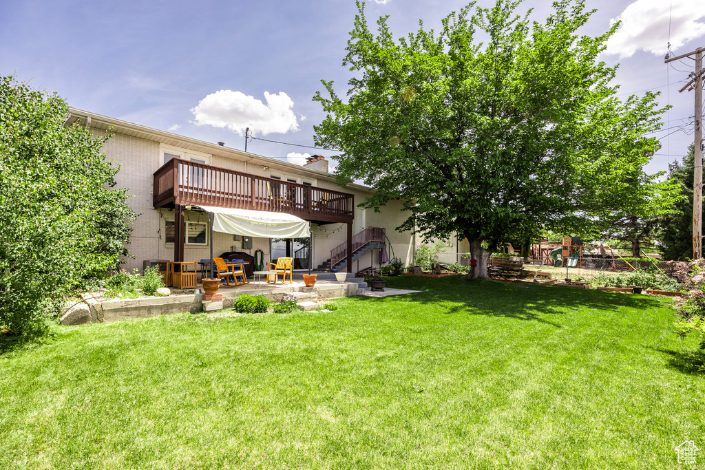 View of grassy yard featuring a patio, a deck, and stairs