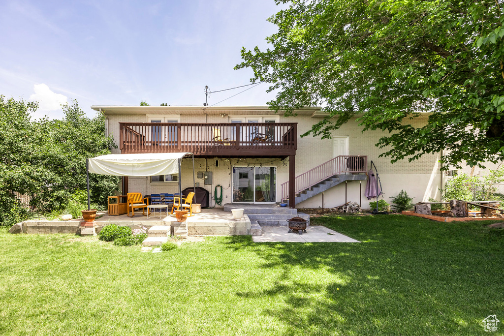 Rear view of property with a patio area, a fire pit, a wooden deck, a lawn, and stucco siding