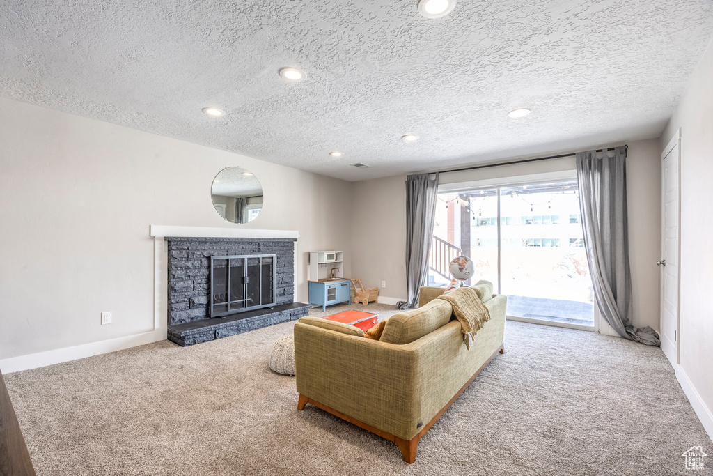 Living room featuring carpet flooring, a fireplace, a textured ceiling, baseboards, and recessed lighting