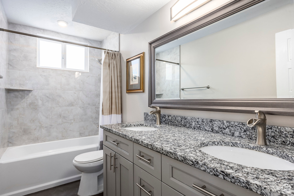 Bathroom with double vanity, shower / tub combo, and toilet