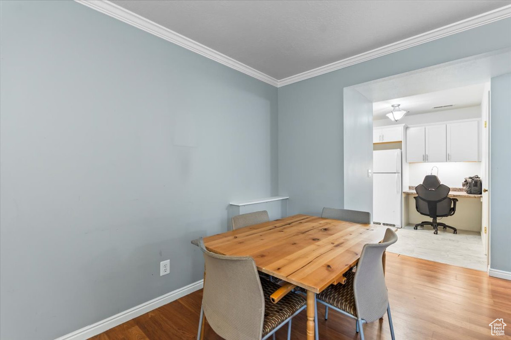 Dining room with light wood finished floors, baseboards, and crown molding
