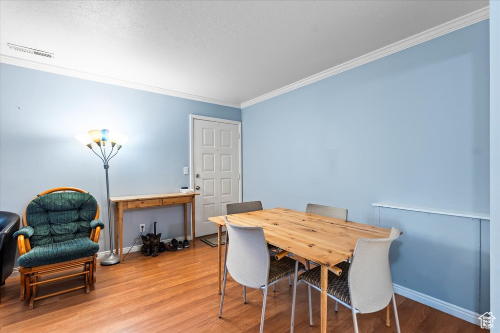 Dining room featuring light wood-type flooring, baseboards, visible vents, and ornamental molding