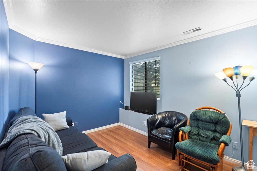 Living area featuring wood finished floors, visible vents, ornamental molding, baseboards, and a textured ceiling