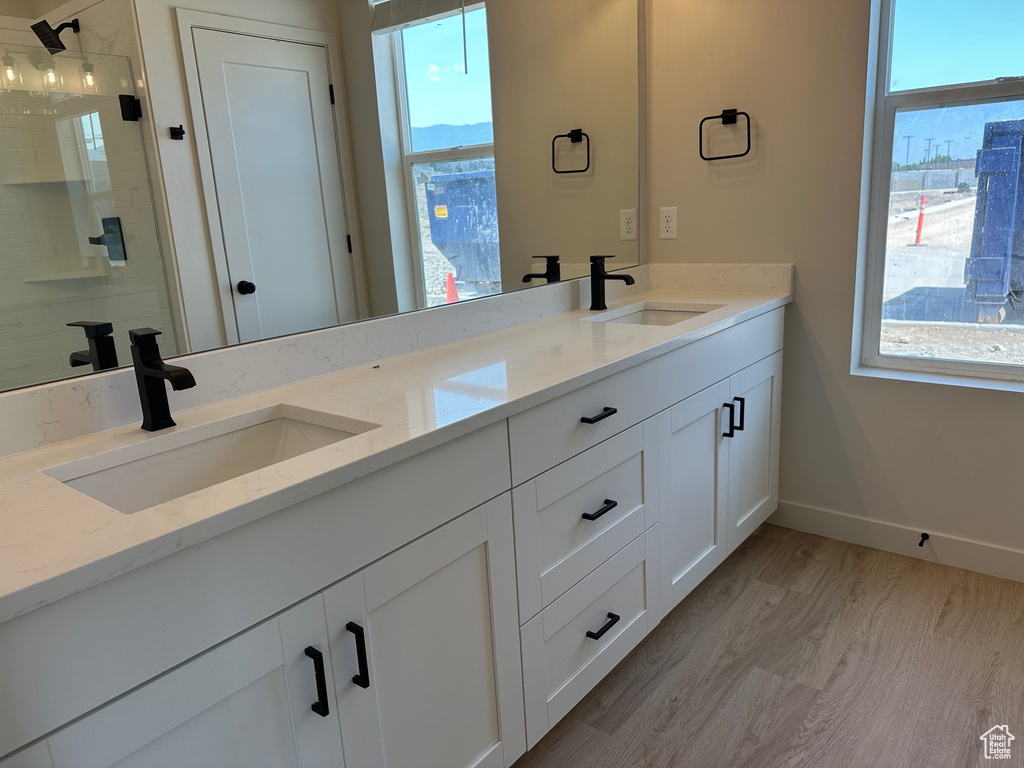 Bathroom featuring double vanity, plenty of natural light, tiled shower, and wood finished floors