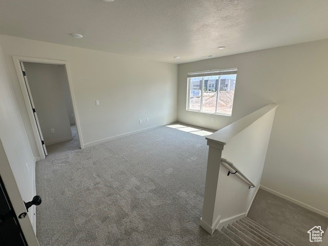Carpeted spare room with a textured ceiling and baseboards