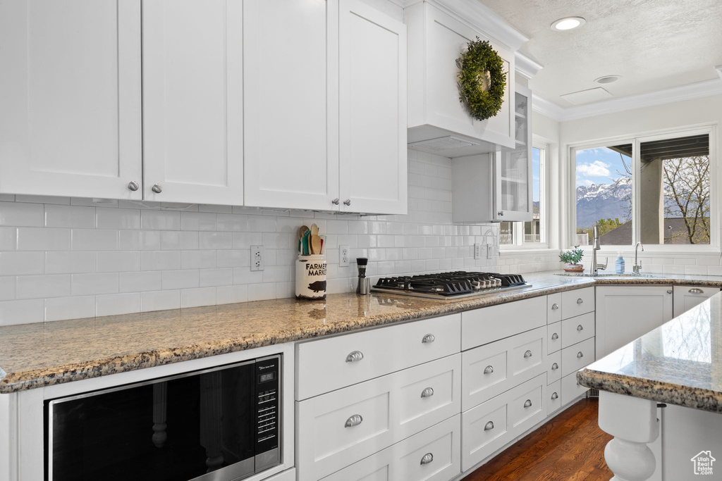 Kitchen with white cabinets, stainless steel gas cooktop, built in microwave, crown molding, and light stone countertops
