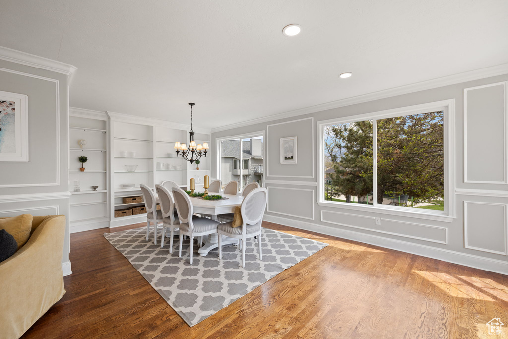 Dining room featuring wood finished floors, an inviting chandelier, built in shelves, and crown molding