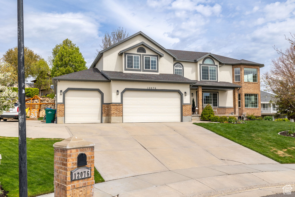 View of front facade with stucco siding, a front lawn, driveway, and brick siding