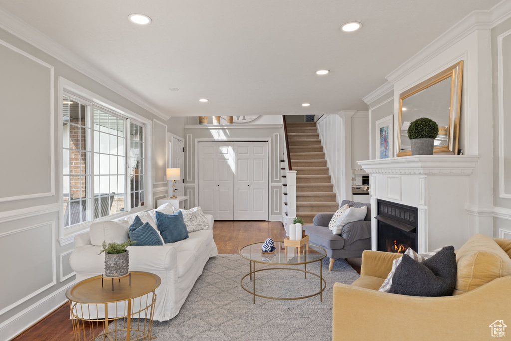 Living room with wood finished floors, recessed lighting, ornamental molding, and a decorative wall