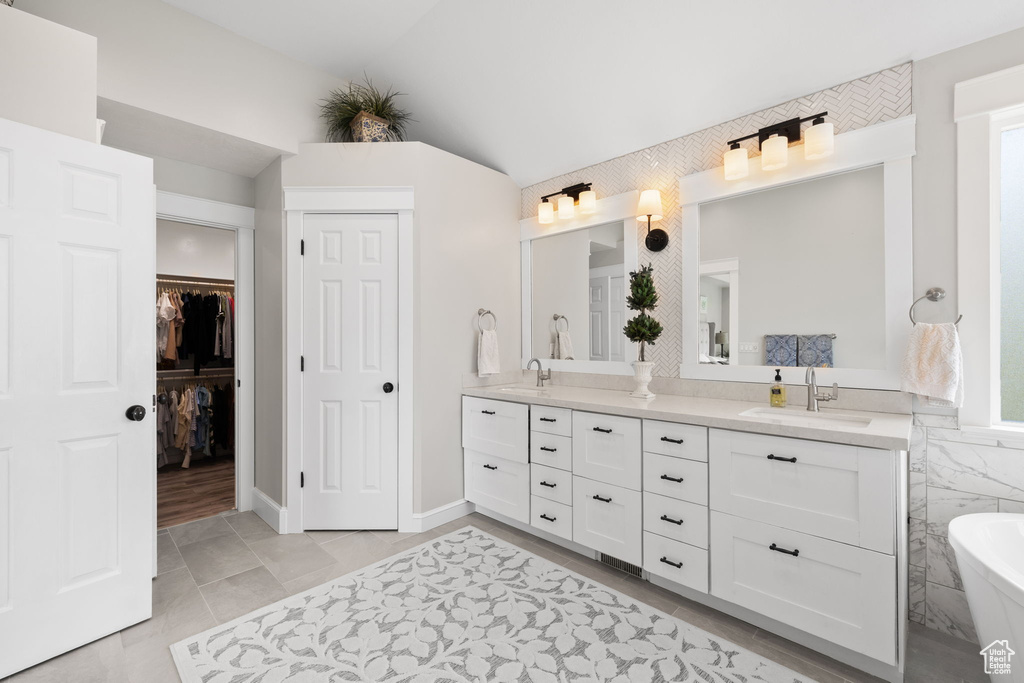 Bathroom with lofted ceiling, a sink, double vanity, and a freestanding bath