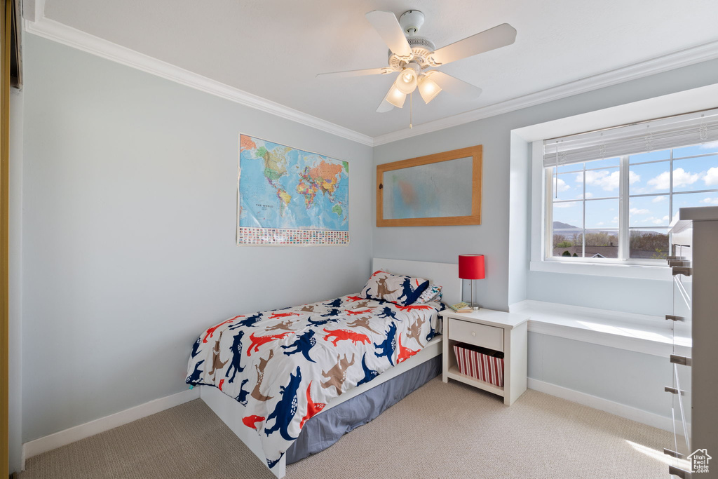 Carpeted bedroom with a ceiling fan, baseboards, and ornamental molding