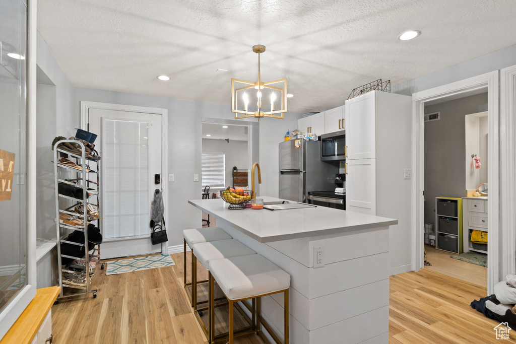 Kitchen featuring white cabinets, stainless steel appliances, light wood finished floors, and an inviting chandelier