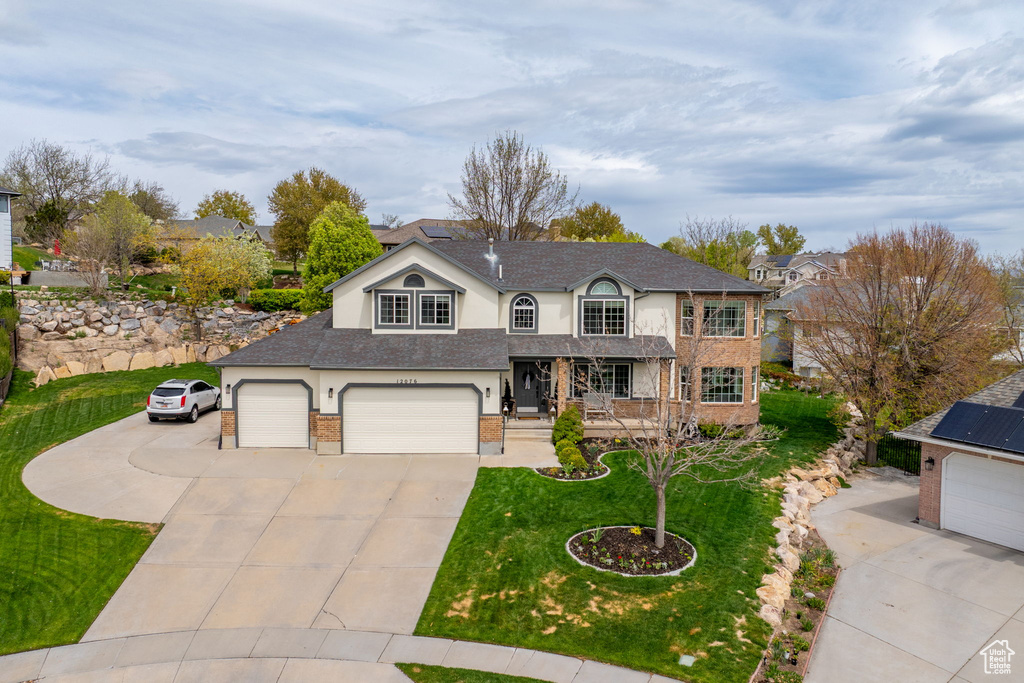 Traditional home featuring concrete driveway, stucco siding, covered porch, brick siding, and a front yard