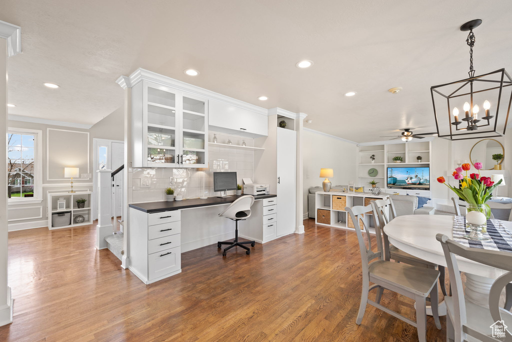 Dining room with built in desk, recessed lighting, wood finished floors, crown molding, and ceiling fan with notable chandelier