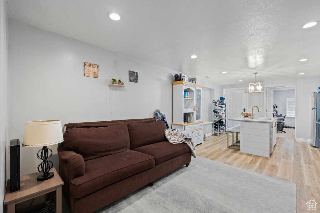 Living room with light wood-style flooring, a textured ceiling, baseboards, recessed lighting, and a notable chandelier
