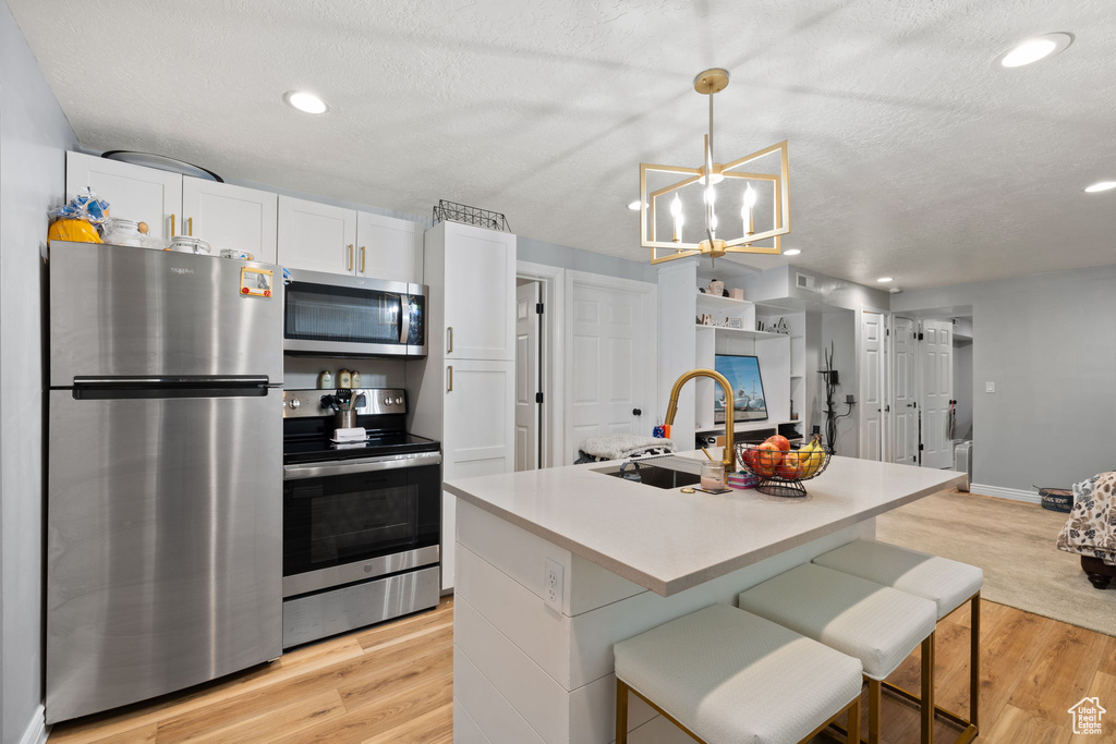 Kitchen with light wood finished floors, stainless steel appliances, light countertops, a sink, and white cabinetry