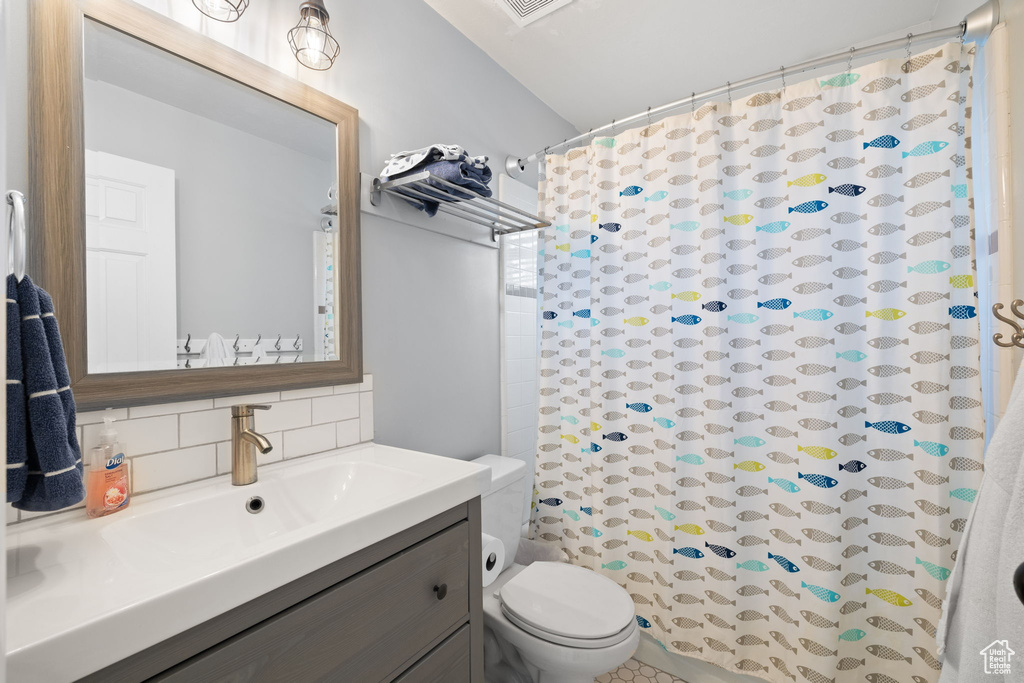 Bathroom featuring toilet, vanity, decorative backsplash, and a shower with curtain