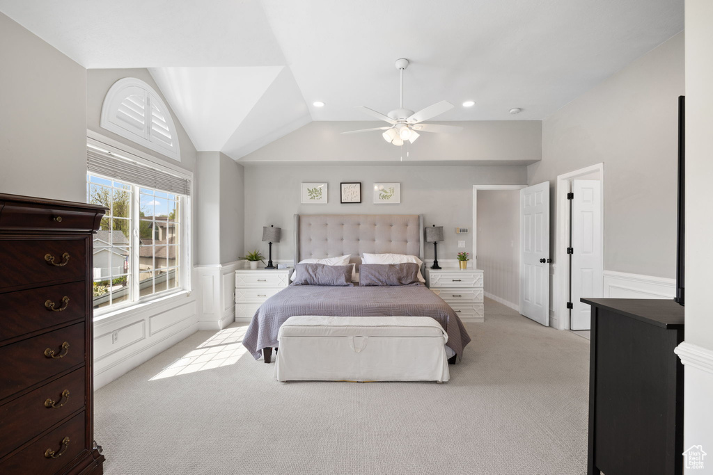 Bedroom with lofted ceiling, a ceiling fan, light carpet, a decorative wall, and wainscoting