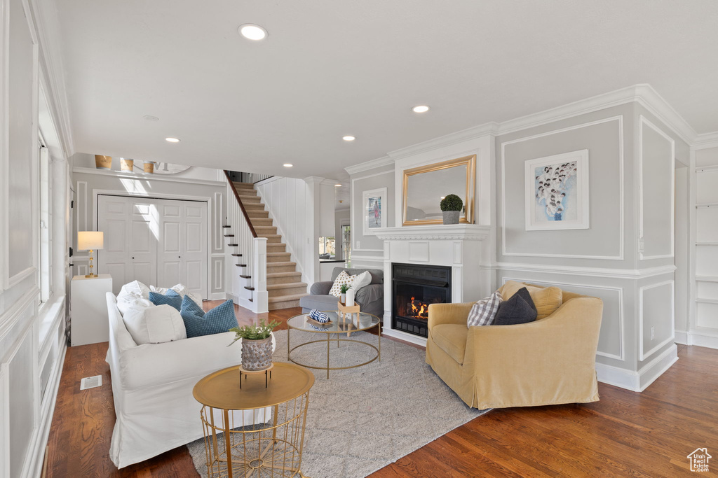 Living room featuring a fireplace with flush hearth, visible vents, wood finished floors, stairway, and a decorative wall
