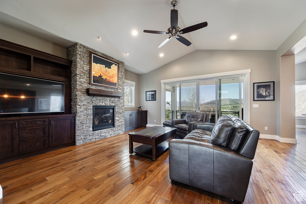 Living room with a ceiling fan, light wood-type flooring, baseboards, a stone fireplace, and lofted ceiling