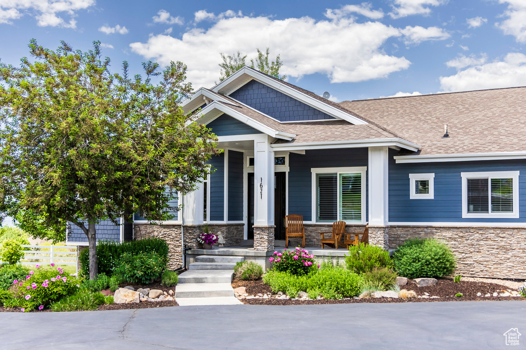 Craftsman-style house featuring stone siding, covered porch, and a shingled roof