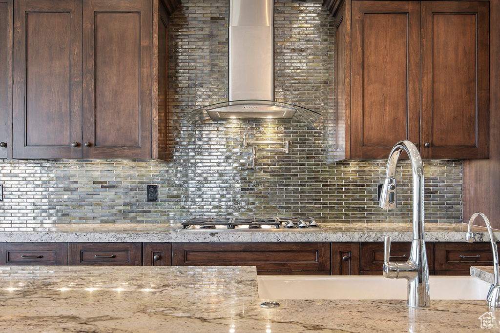 Kitchen featuring wall chimney exhaust hood, stainless steel gas cooktop, decorative backsplash, and light stone counters