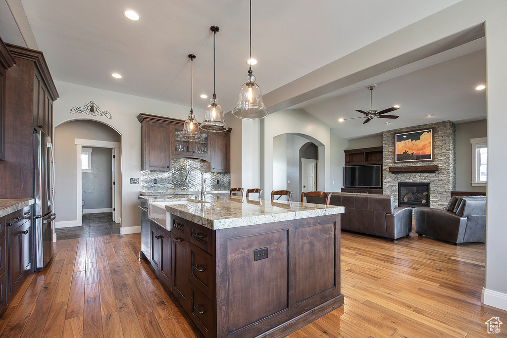 Kitchen featuring arched walkways, freestanding refrigerator, ceiling fan, a sink, and dark brown cabinetry
