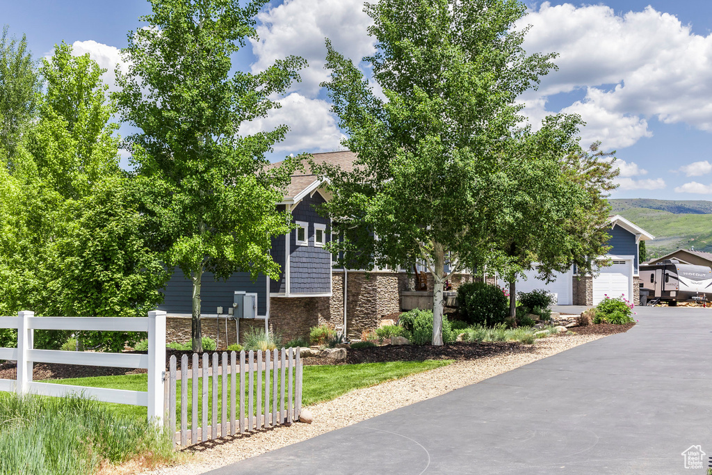 View of property hidden behind natural elements with stone siding, asphalt driveway, and an attached garage