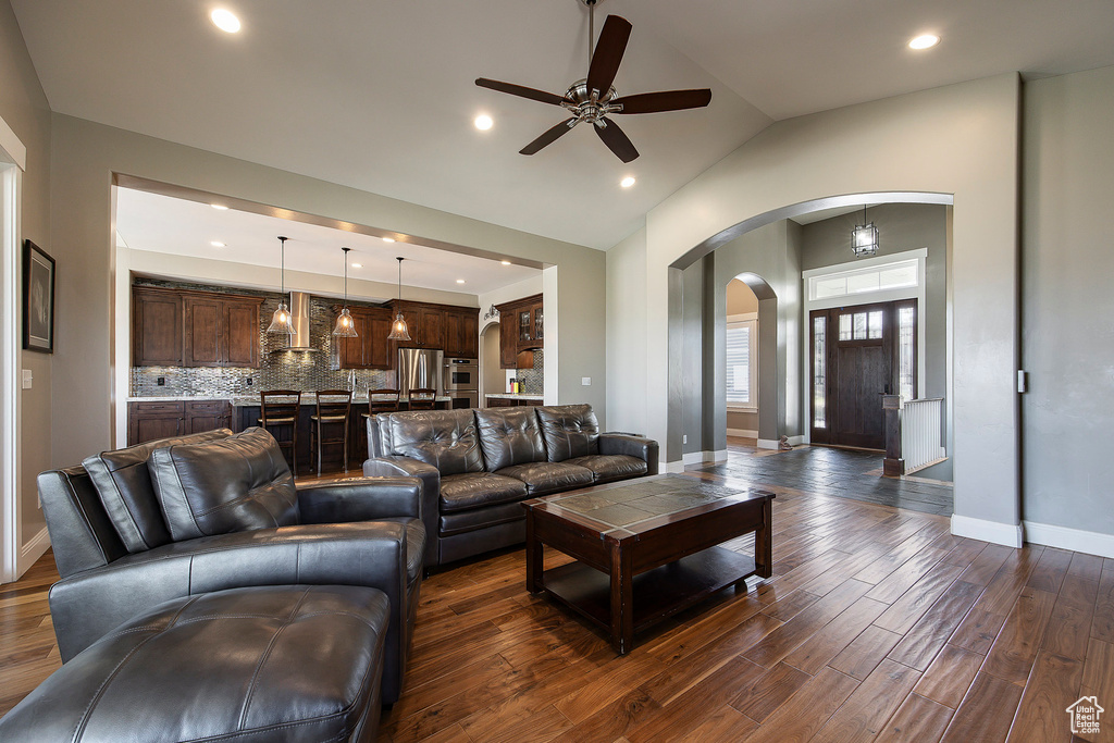 Living room with arched walkways, ceiling fan, dark wood-type flooring, baseboards, and lofted ceiling