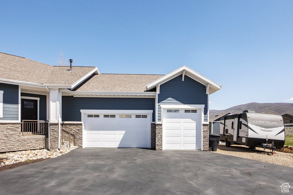 View of front of home with stone siding, an attached garage, asphalt driveway, a shingled roof, and a mountain view
