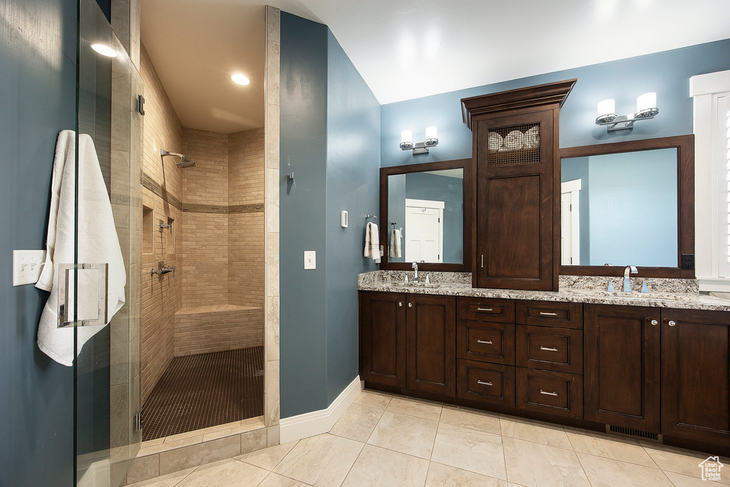 Bathroom featuring a shower stall, double vanity, and baseboards