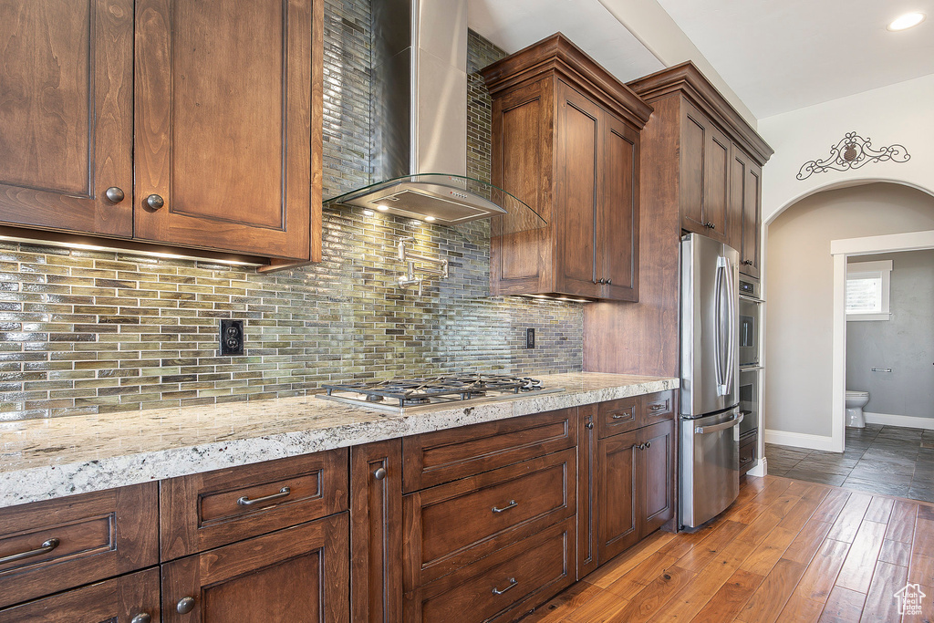 Kitchen with wall chimney range hood, appliances with stainless steel finishes, arched walkways, and backsplash