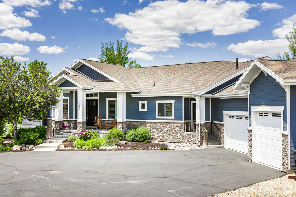 Craftsman-style home featuring driveway, stone siding, a porch, and an attached garage