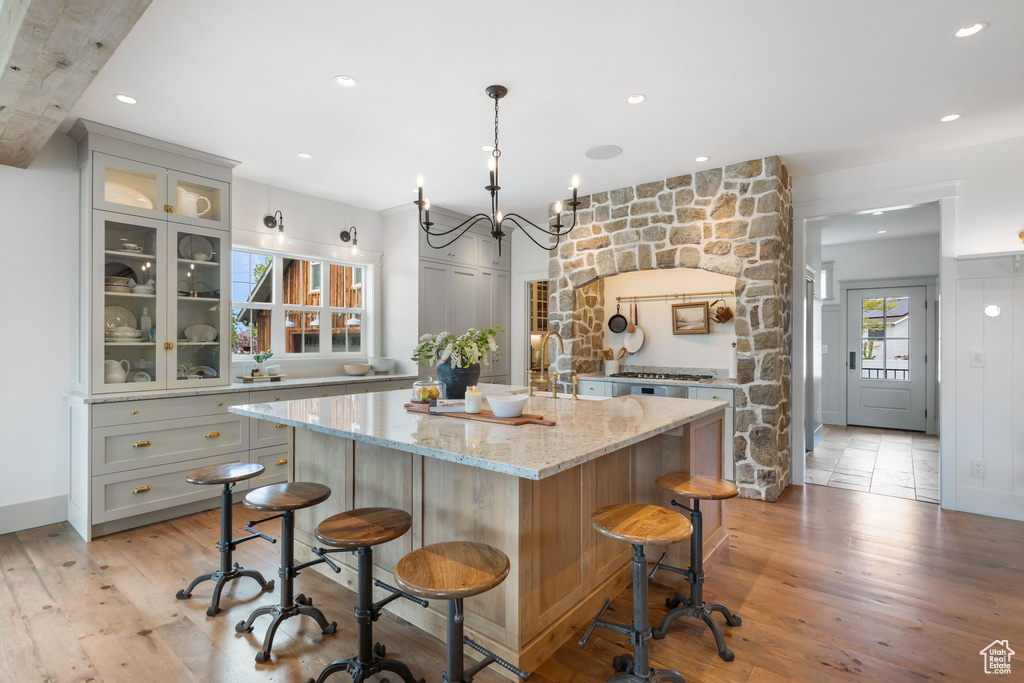 Kitchen featuring a kitchen bar, light stone countertops, a kitchen island with sink, and glass insert cabinets