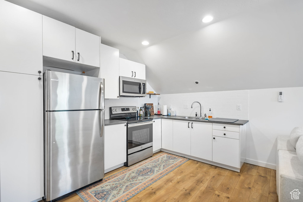 Kitchen featuring light wood-type flooring, dark countertops, a sink, and appliances with stainless steel finishes