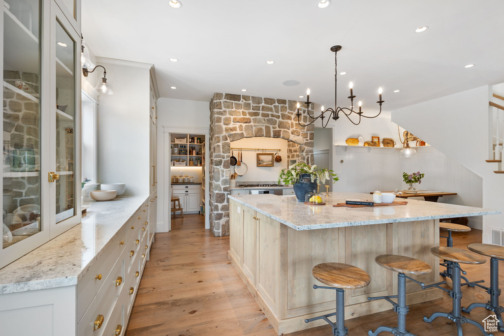 Kitchen featuring light stone counters, a kitchen breakfast bar, glass insert cabinets, a large island, and light wood-type flooring