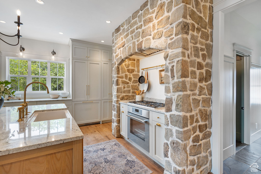 Kitchen featuring light stone countertops, light wood finished floors, stainless steel appliances, and a sink