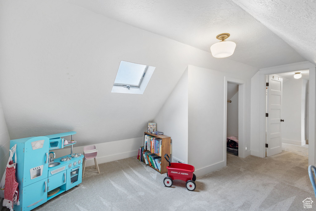 Playroom featuring vaulted ceiling with skylight, carpet, a textured ceiling, and baseboards