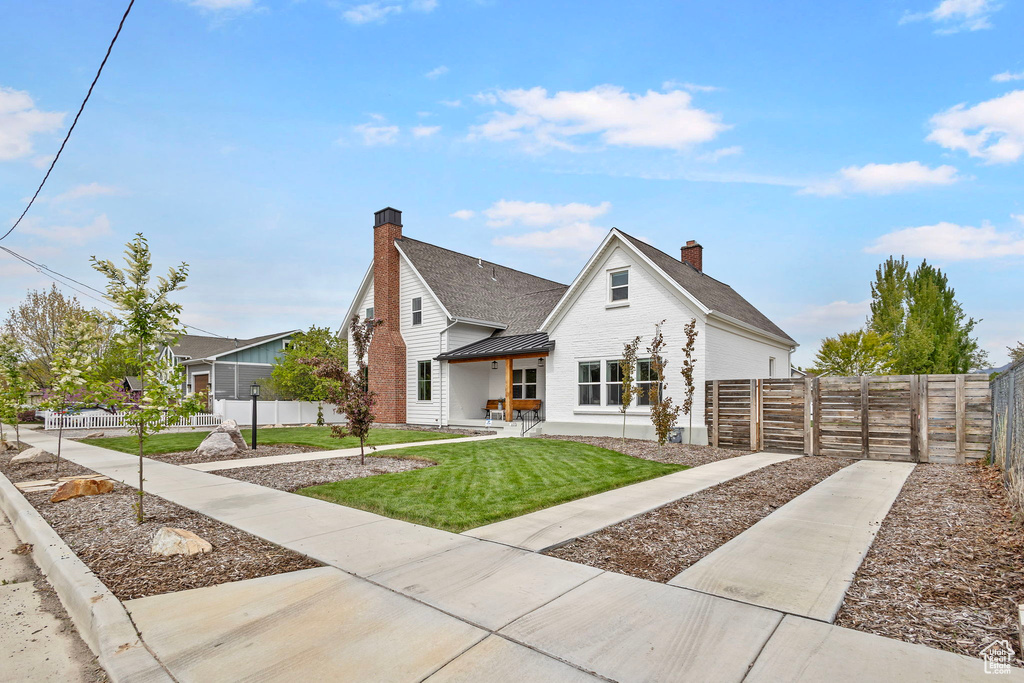 View of front of property featuring a chimney, brick siding, a front yard, and fence private yard